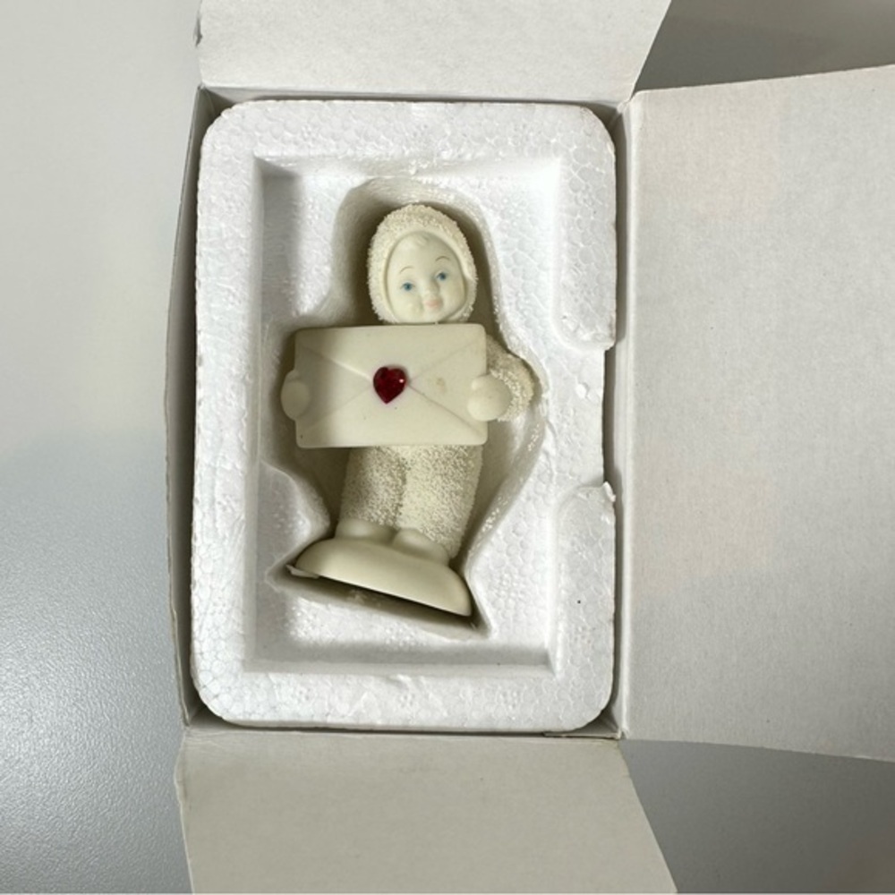 DEPARTMENT 56 SNOW BABY HOLDING ENVELOPE WITH RED HEART JEWEL BIRTHSTONE